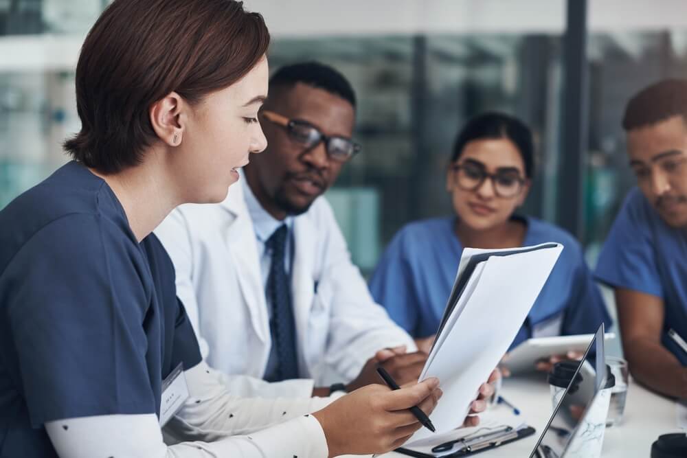 A health care team reviews competency assessment tools around a table.