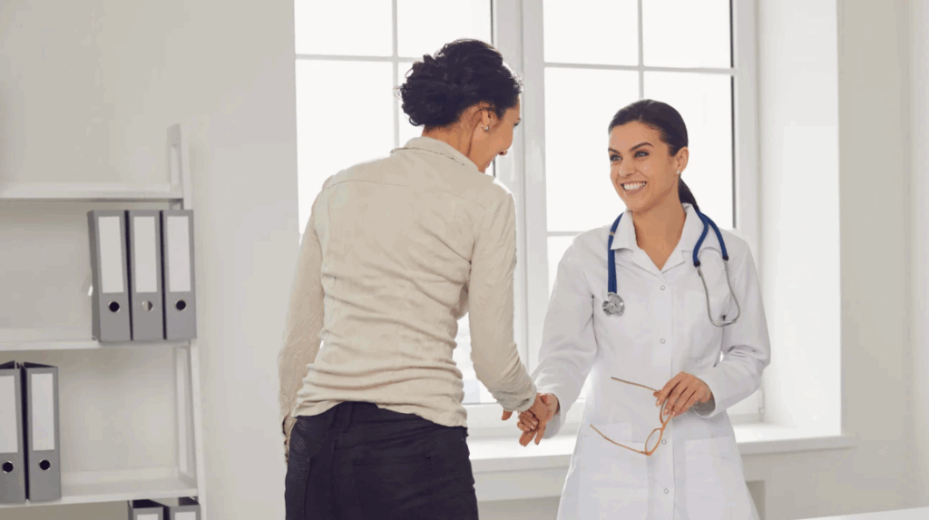 Smiling female doctor shaking hands with a business professional in a bright medical office, symbolizing trust, partnership, and quality care.